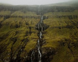 Alta cascata che scende lungo un versante erboso